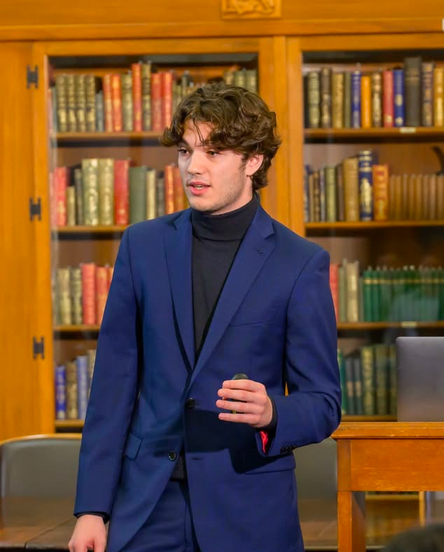 Jonathan Zanzuri speaking, wearing a navy jacket and black turtleneck